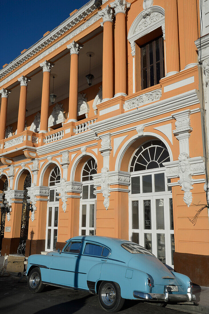 Kuba,santiago,Ein altes blaues amerikanisches Auto parkt vor einem schönen orangefarbenen Kolonialhaus.