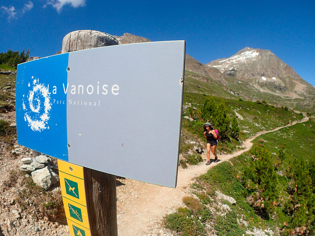 France,Alps,savoie,a woman in shorts is hikking on  a mountain trail behind the sign marking the limits of the Vanoise national park here at the Barbier pass 2300m