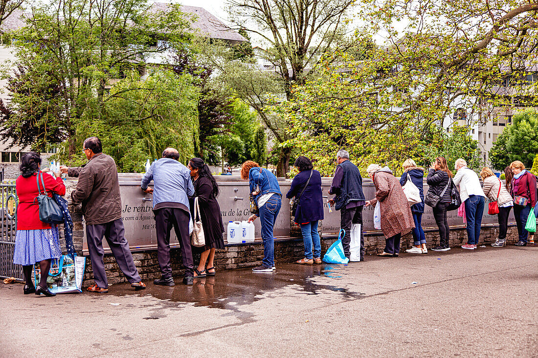 LOURDES - 15. JUNI 2019: Pilger, die in der Nähe der Grotte von Lourdes Flaschen mit Weihwasser füllen