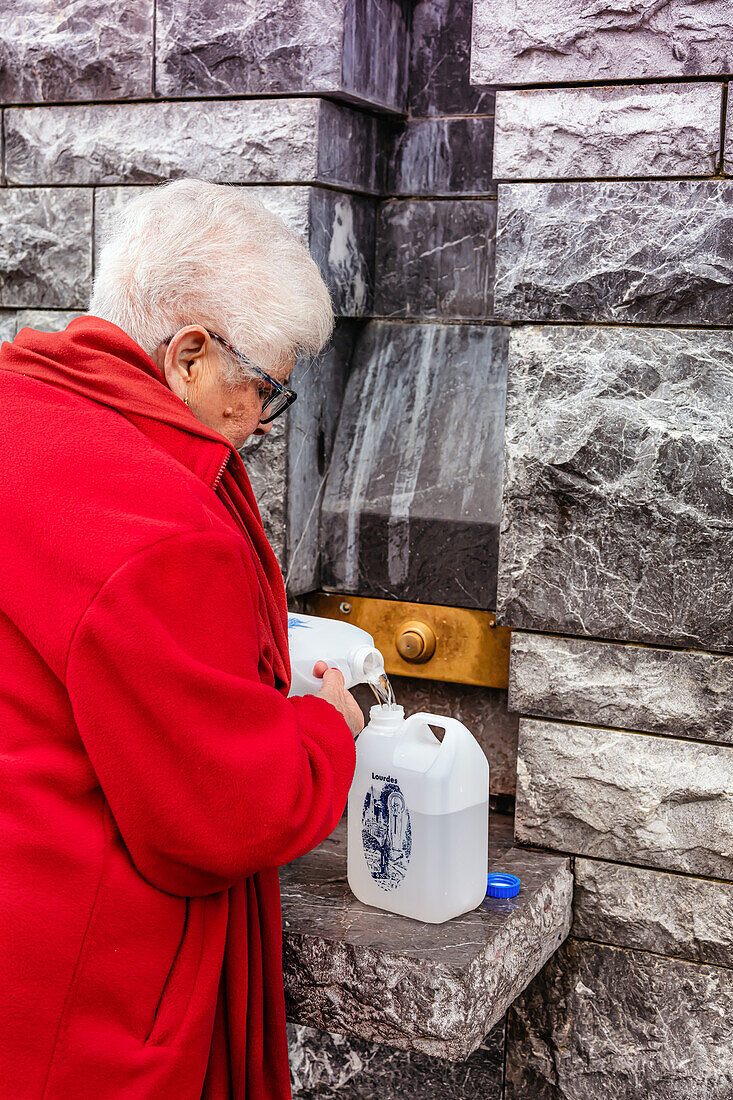 LOURDES - 15. JUNI 2019: Blick auf einen Gläubigen, der eine Flasche mit Weihwasser füllt, Lourdes, Frankreich