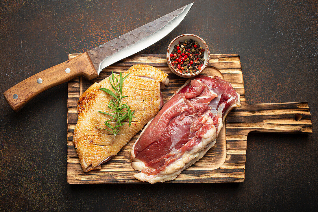 Two raw duck breast fillets with rosemary and peppercorns