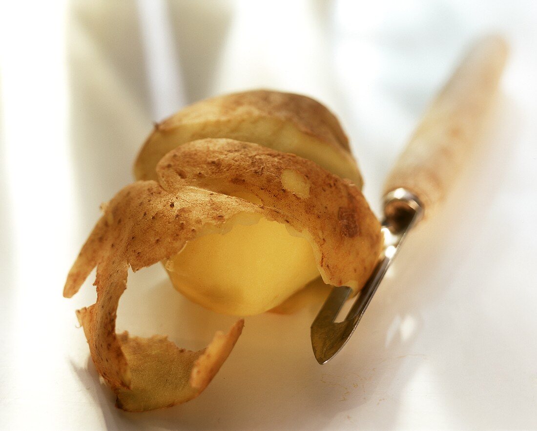 Half-peeled potato (Italian Sieglinde) with potato peeler