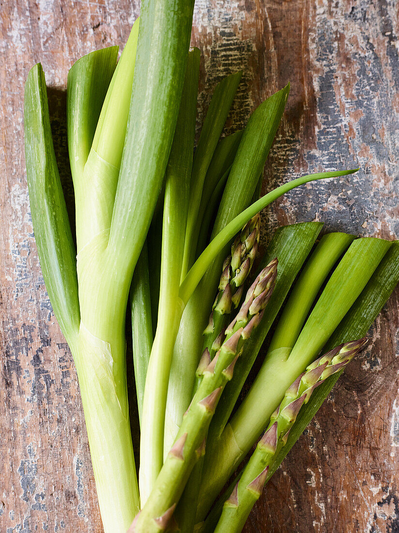 Frühlingszwiebeln und grüner Spargel auf rustikalem Untergrund