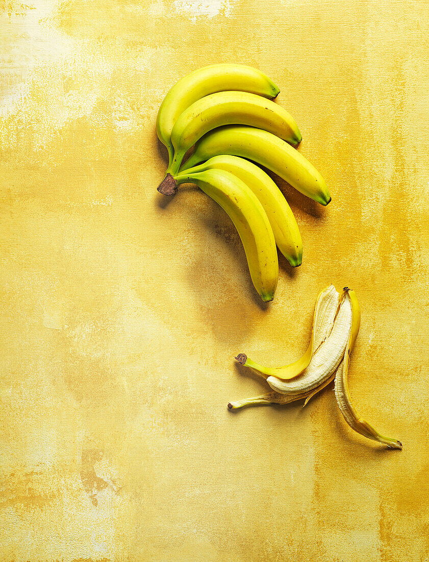 Bananenbüschel und geschälte Banane auf gelbem Hintergrund