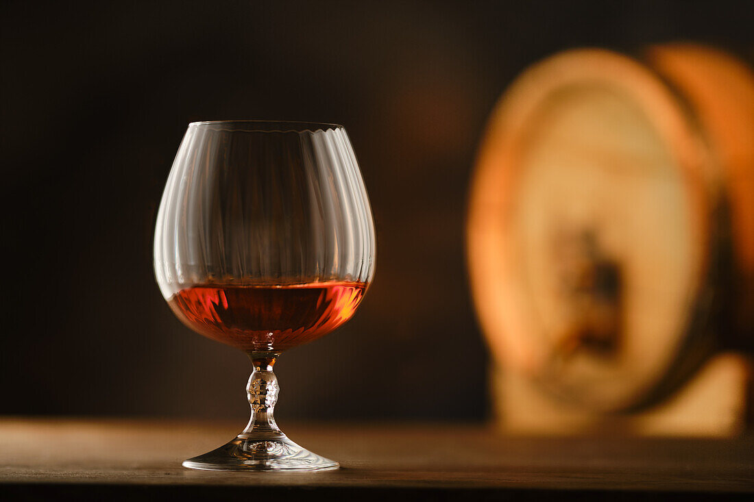 A glass of cognac in front of an old oak barrel