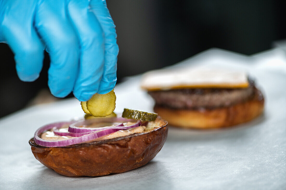 Cook placing pickles on burger