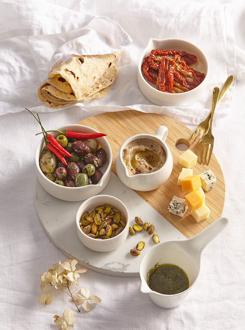 Antipasti-Platte mit Oliven, Käse, getrockneten Tomaten, Pistazien und Dips