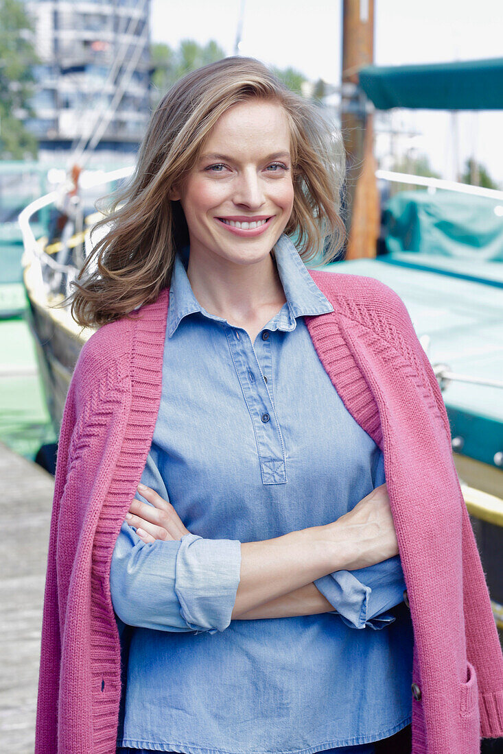 Young woman in jeans outfit and pink cardigan at the harbor