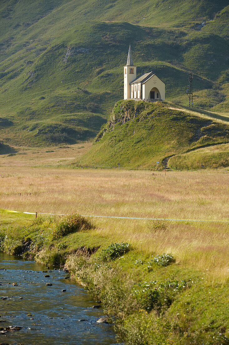 Kirche auf Hügel mit Bergkulisse und Bach bei Formazza, Provinz Verbano-Cusio-Ossola, Region Piemont, Italien