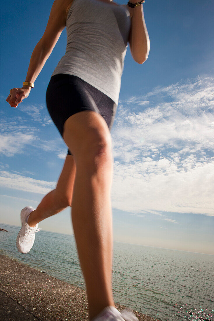 Woman running by waterfront, headless, low angle view