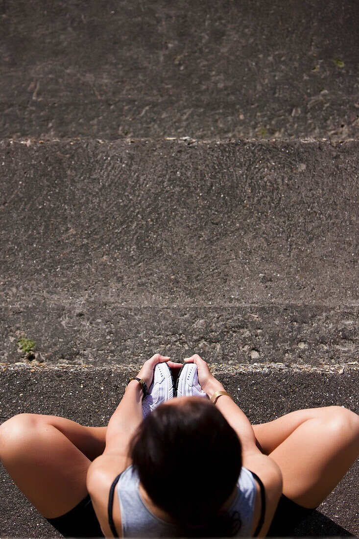 Elevated view of a woman sitting on concrete steps holding her feet