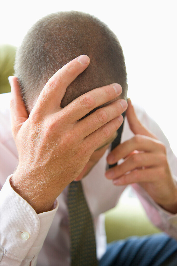 Close up of Businessman with Head in Hands Using Cell Phone