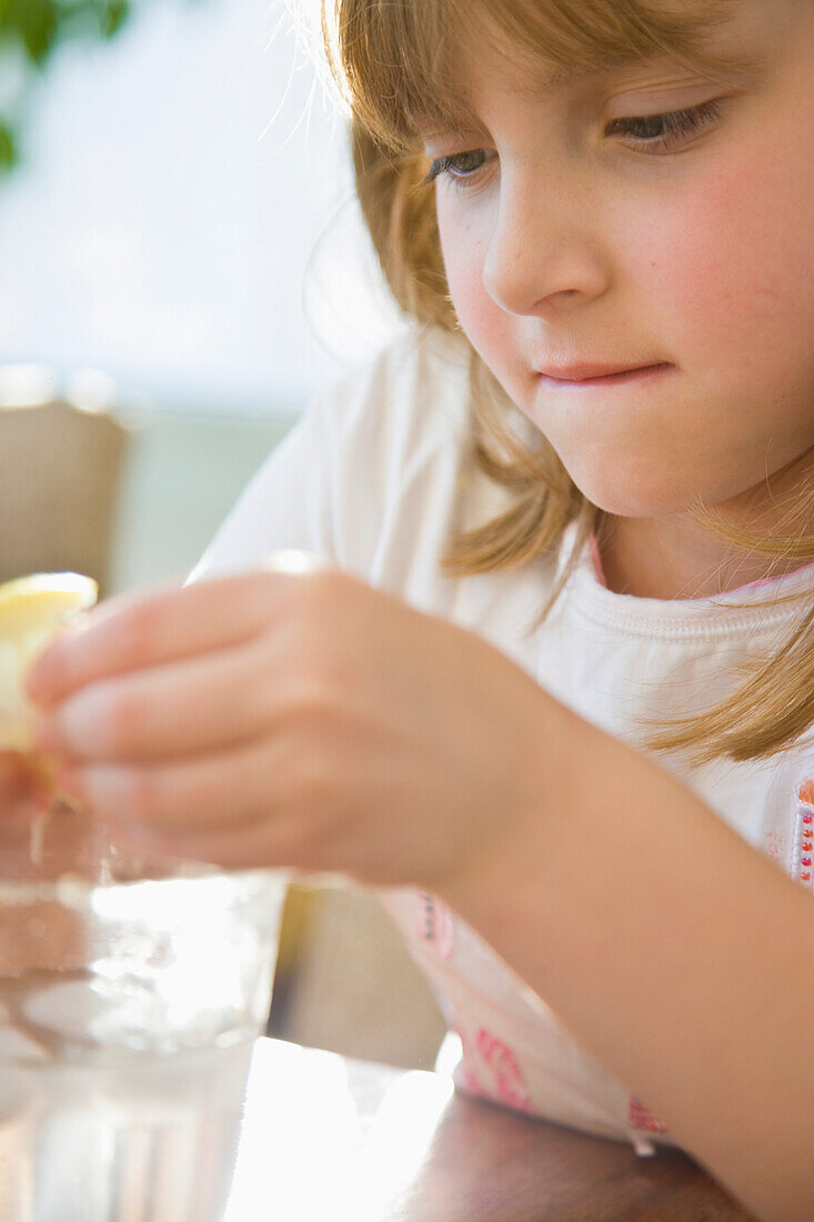 Mädchen, das mit einer Zitronenscheibe über einem Glas Wasser spielt