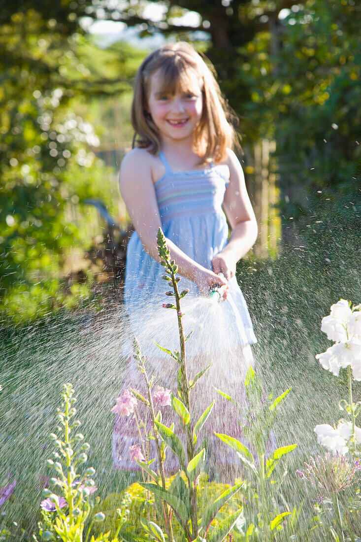 Junges Mädchen bewässert Blumen mit Gartenschlauch