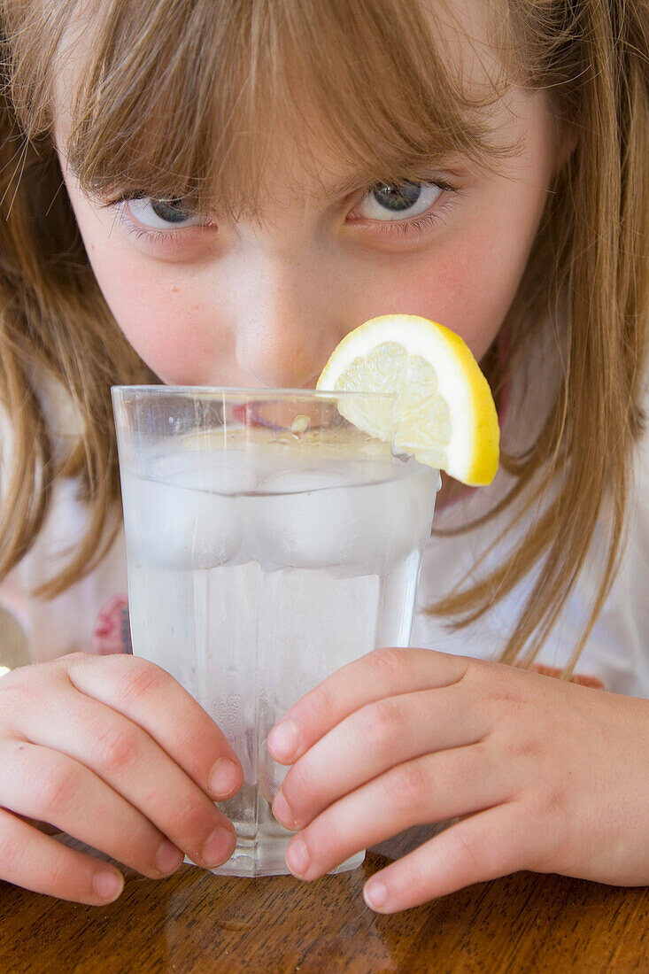 Mädchen trinkt Wasser mit Eis und Zitrone