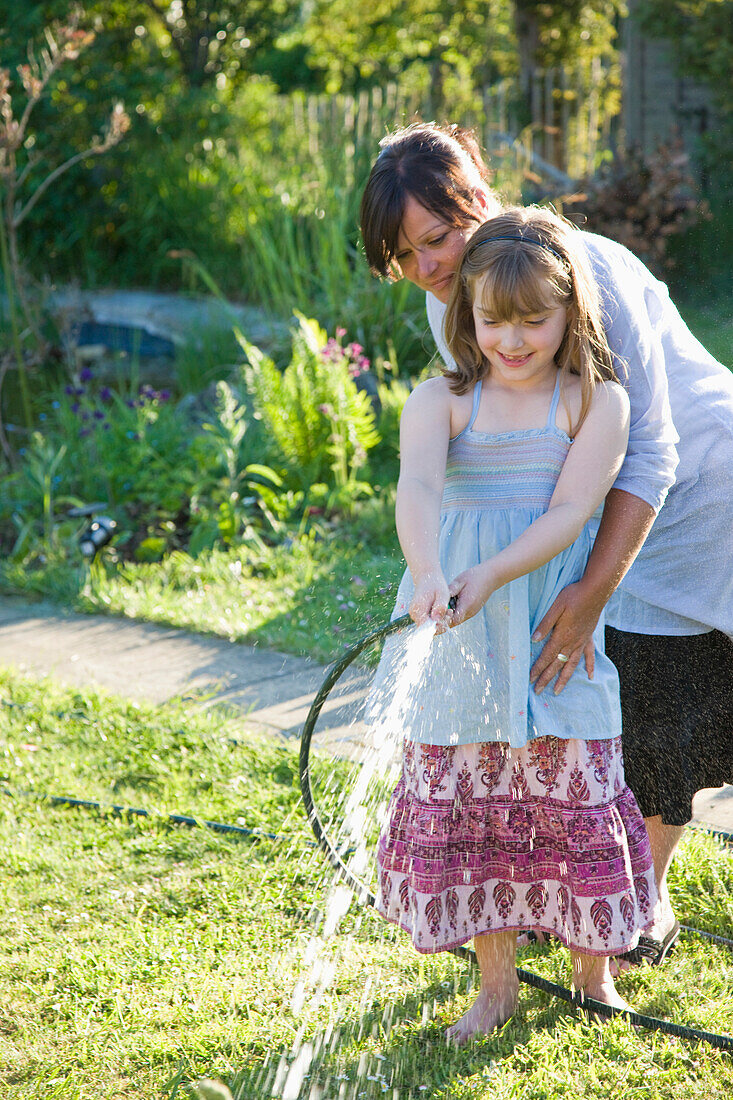 Mutter und Tochter beim Bewässern des Rasens mit einem Gartenschlauch