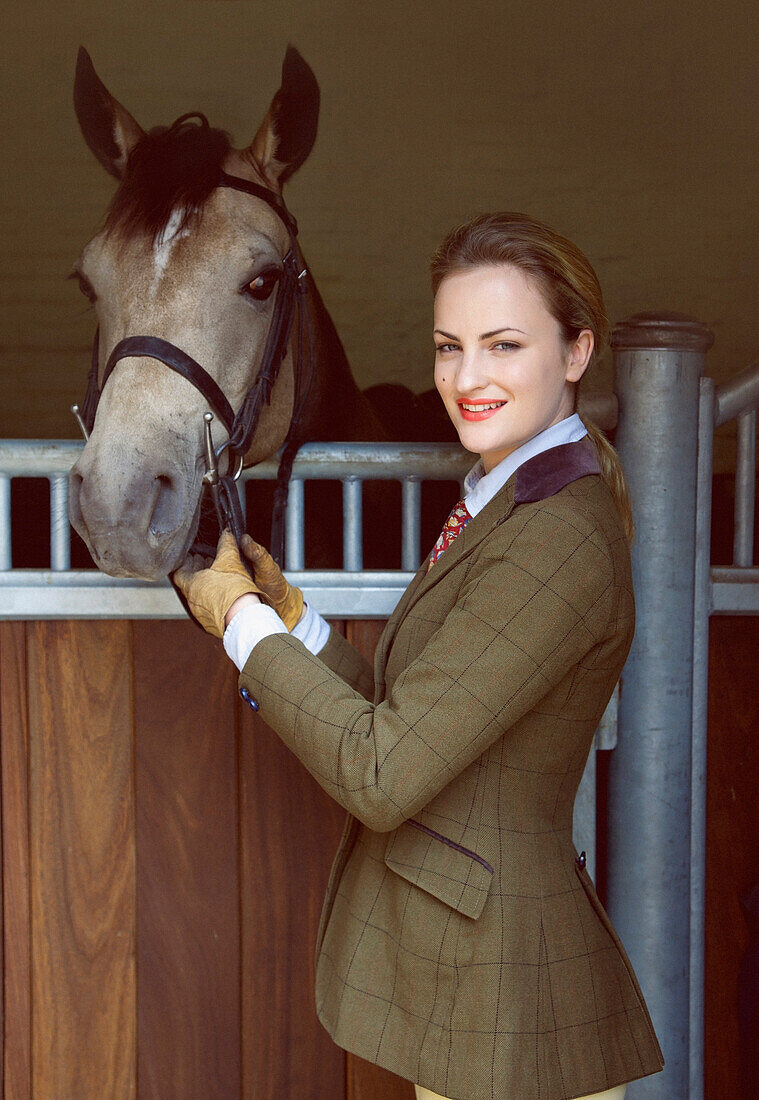 Frau mit Pferd vor einem Stall stehend