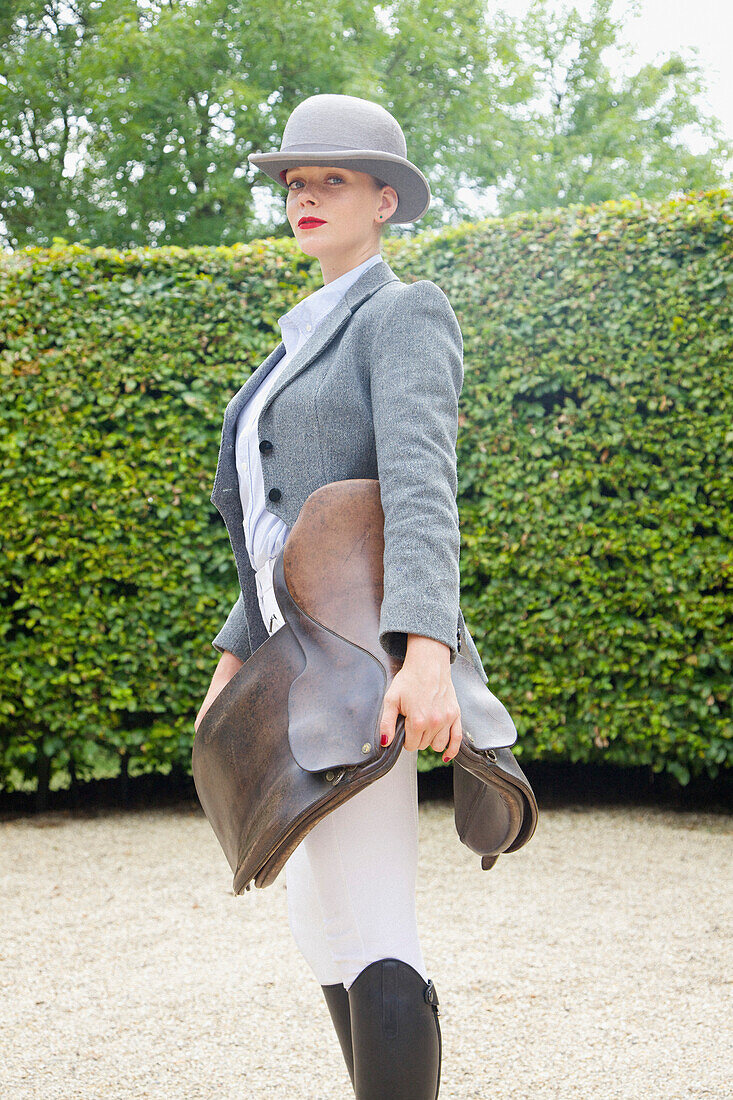 Woman in Riding Outfit Holding Saddle