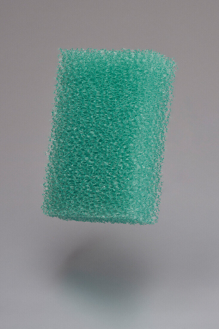 Turquoise colored textured cleaning sponge floating midair on gray background