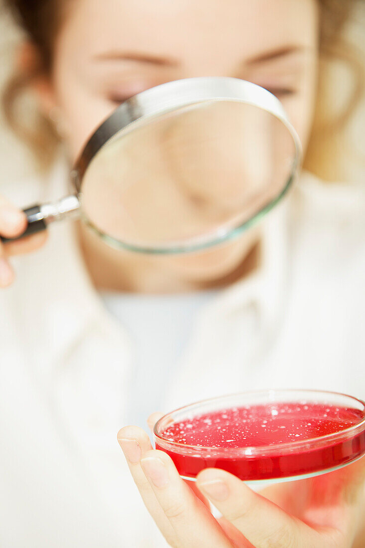 Schoolgirl Examining Cell Culture in Petri Dish with Magnifying Glass