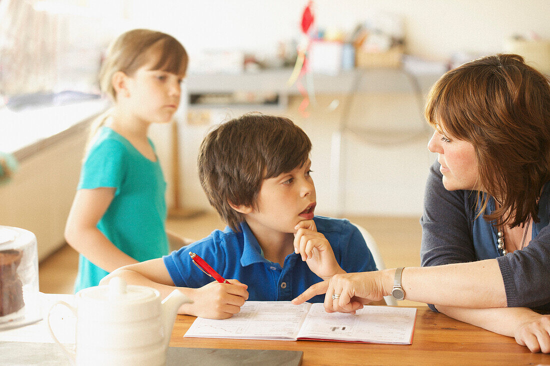 Mother and Son Doing Homework at Kitchen Table, Daughter in background