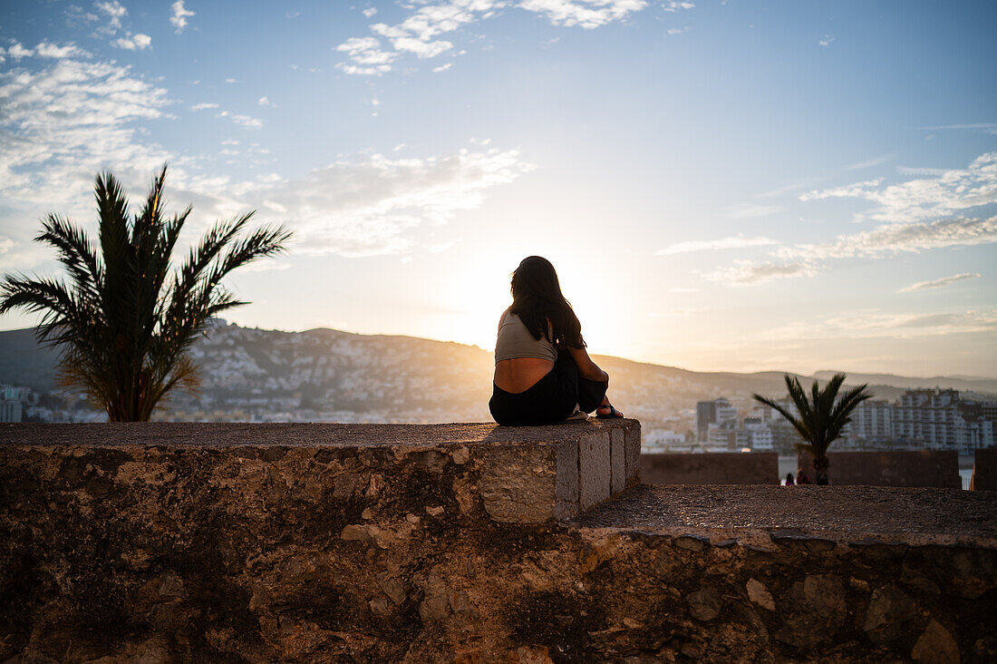 Junge Frau genießt den Sonnenuntergang von der Stadtmauer der Burg Papa Luna in Peñiscola, Castellon, Valencianische Gemeinschaft, Spanien