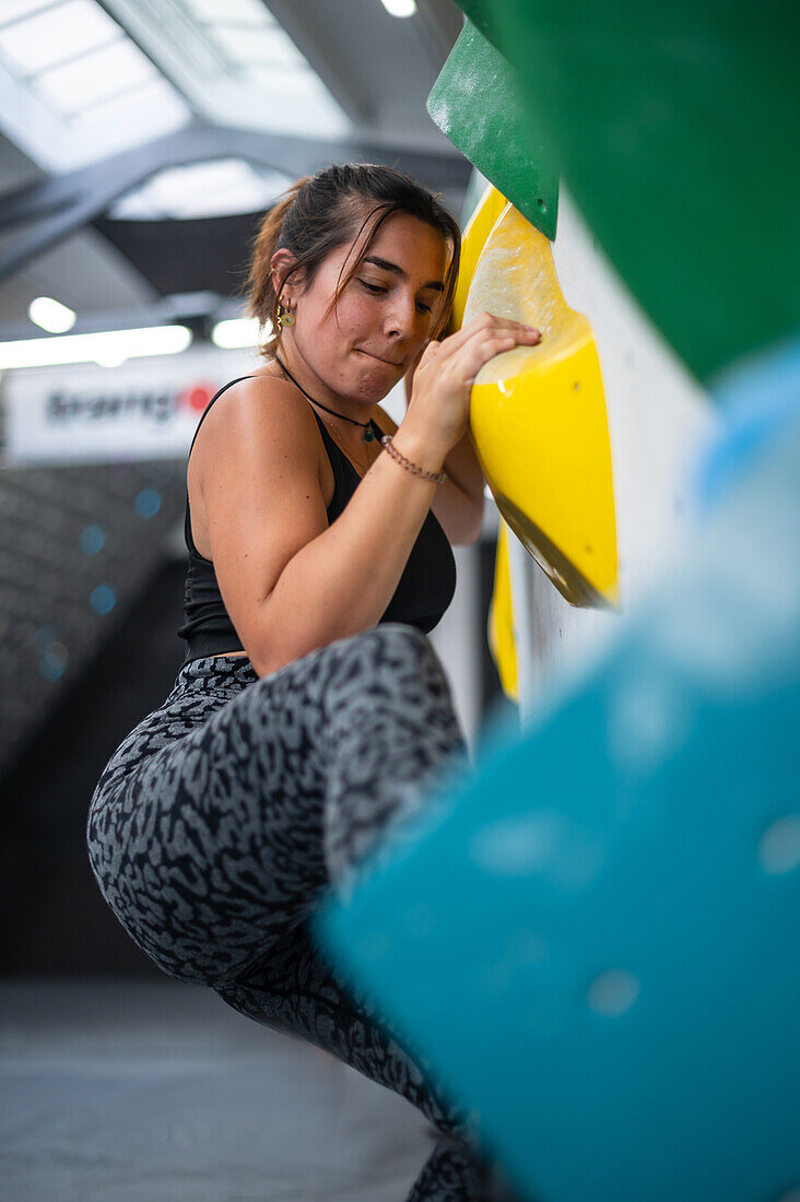 Young man in her twenties climbing on a climbing wall indoors