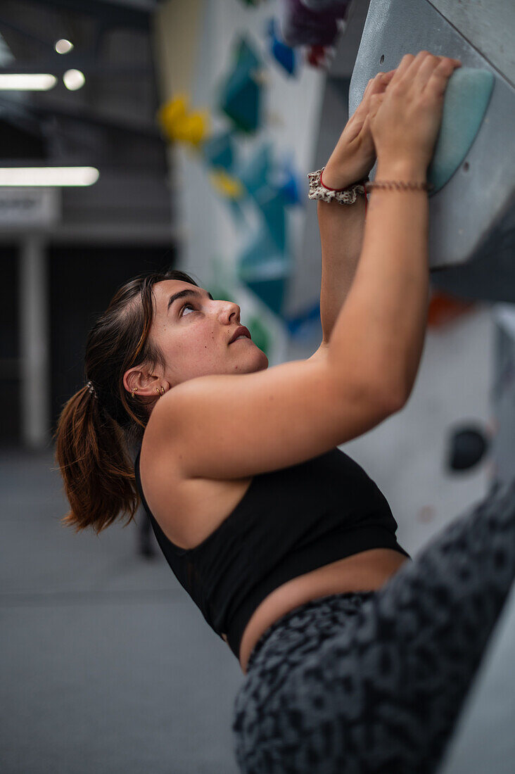 Young man in her twenties climbing on a climbing wall indoors