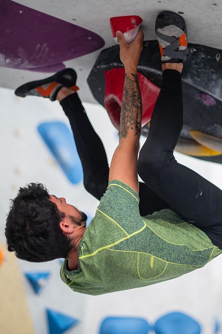 Junger Mann in den Zwanzigern beim Klettern an einer Kletterwand in einer Halle