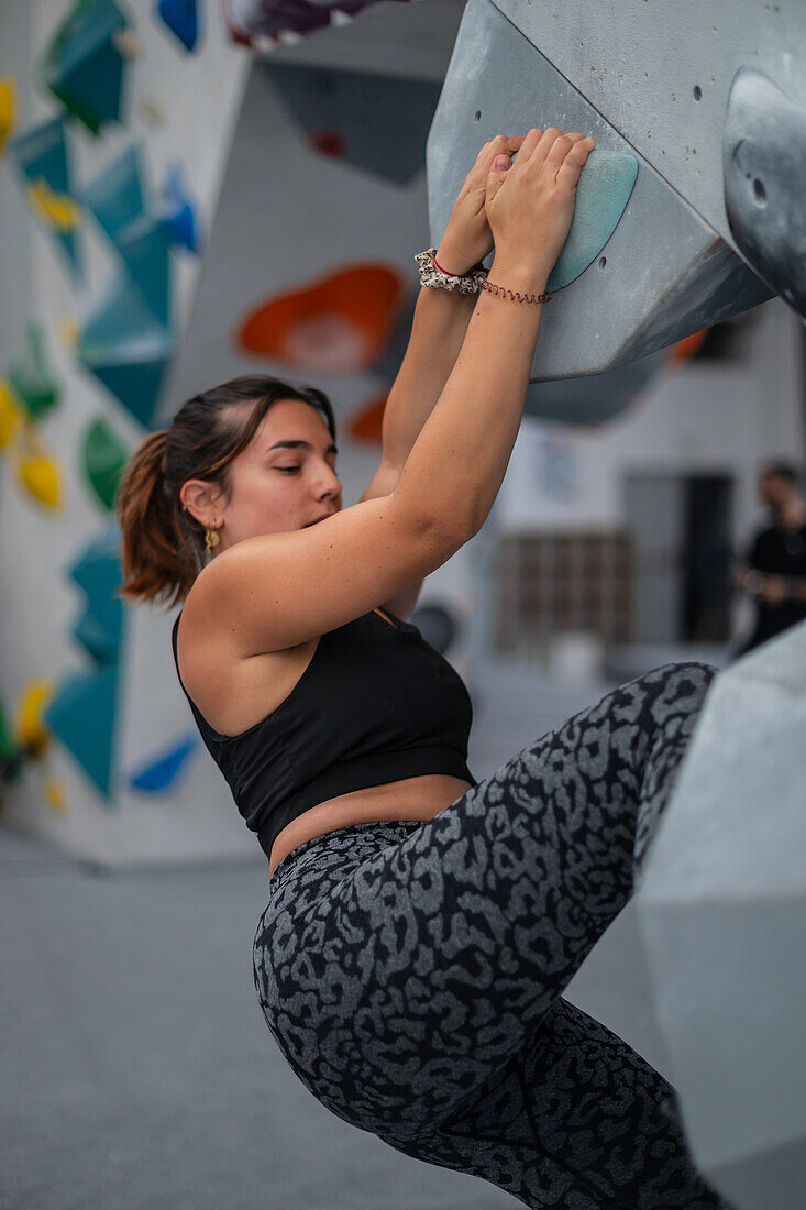 Young man in her twenties climbing on a climbing wall indoors