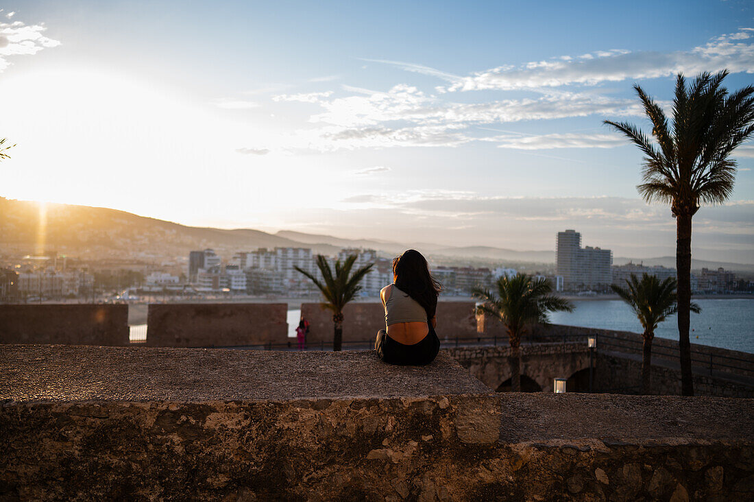 Young woman enjoying the sunset from the city walls of Papa Luna castle in Peñiscola, Castellon, Valencian Community, Spain