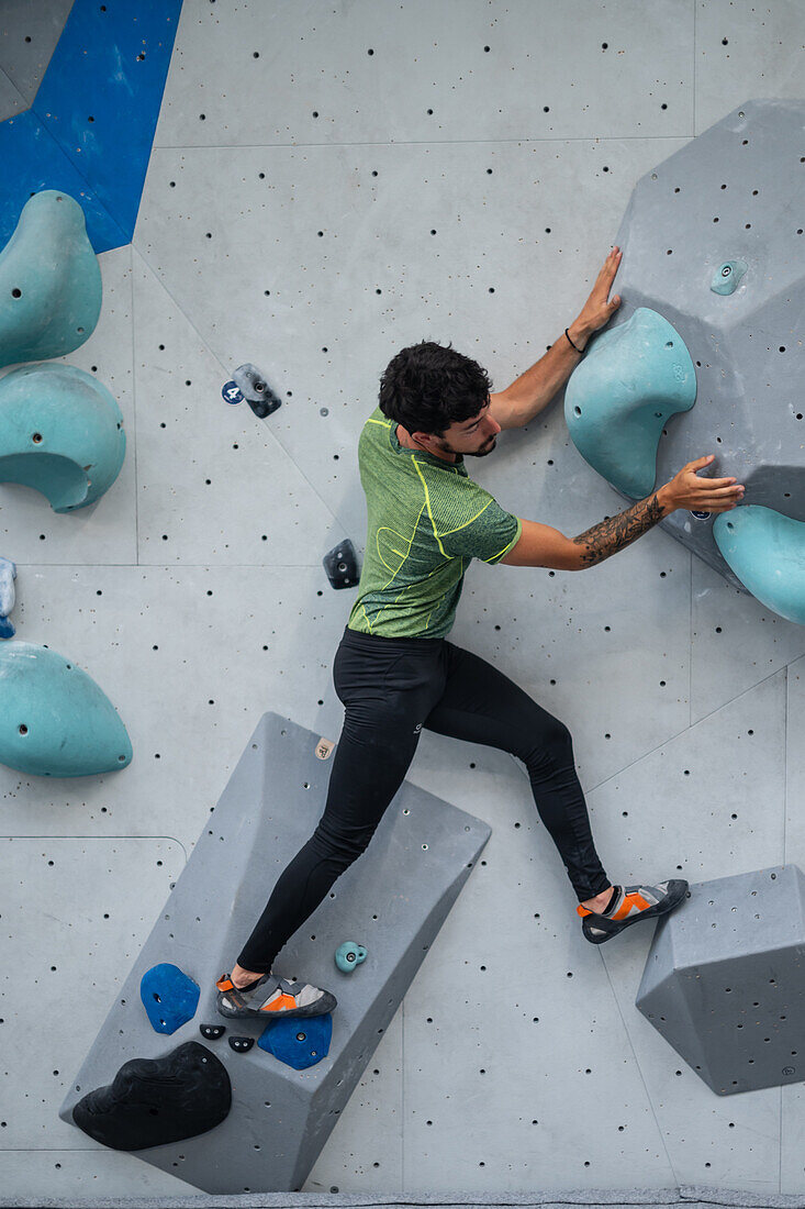 Junger Mann in den Zwanzigern beim Klettern an einer Kletterwand in einer Halle