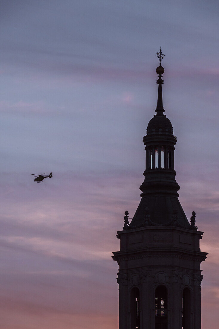 Hubschrauber fliegt neben einem der Türme der Kathedrale-Basilika Unserer Lieben Frau von der Säule bei Sonnenuntergang, Zaragoza, Spanien