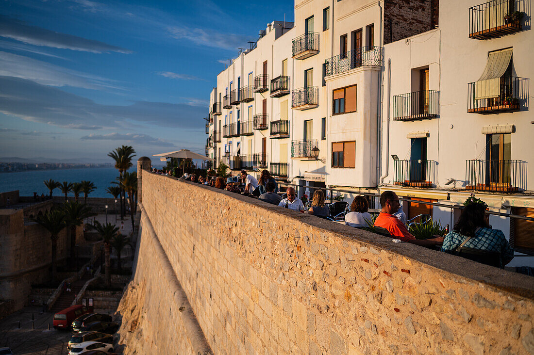 Besucher genießen den Sonnenuntergang von einem Restaurant auf der Stadtmauer der Burg Papa Luna in Peñiscola, Castellon, Valencianische Gemeinschaft, Spanien