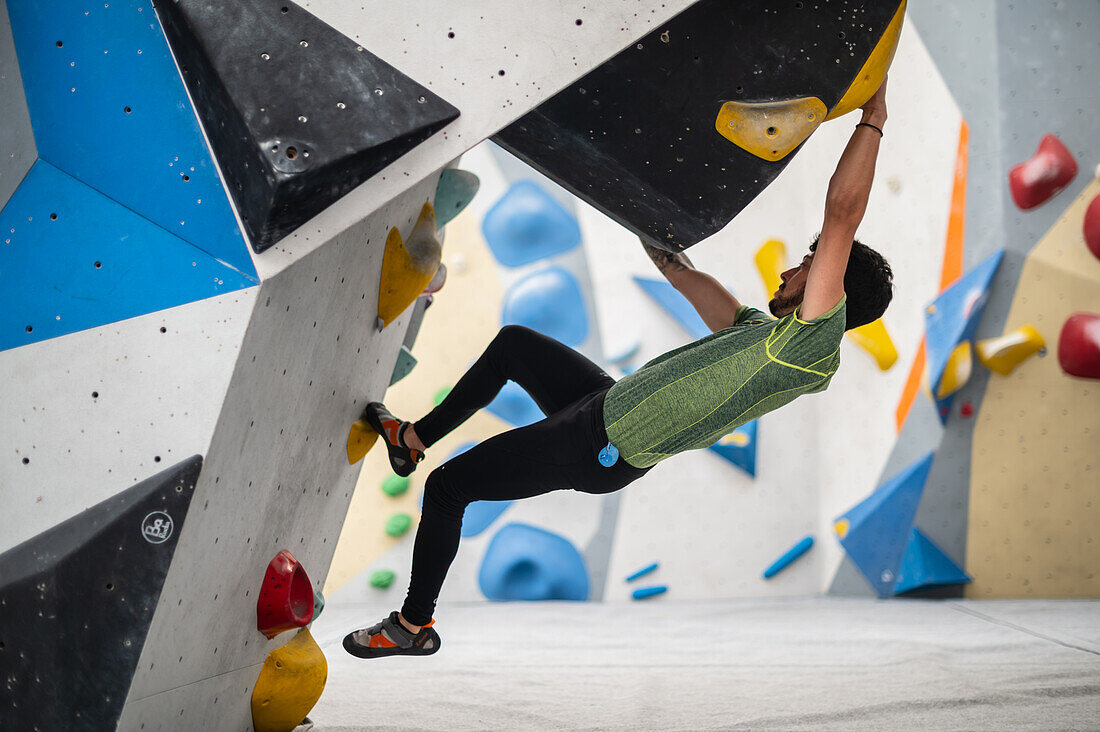 Junger Mann in den Zwanzigern beim Klettern an einer Kletterwand in einer Halle