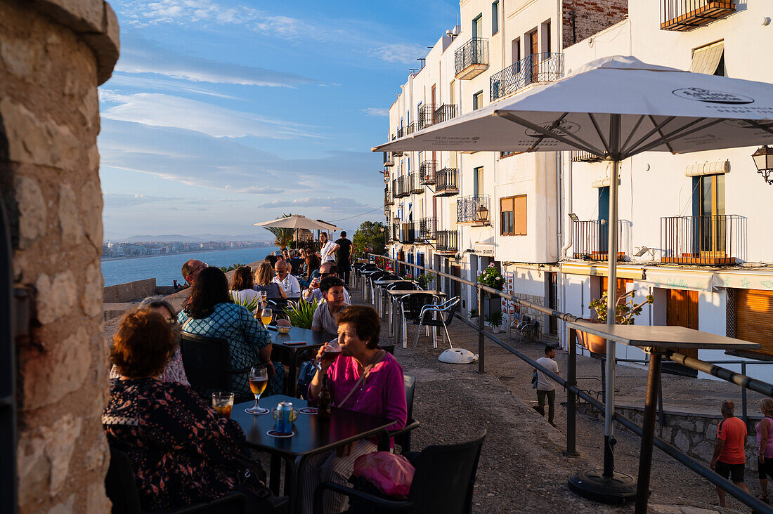 Besucher genießen den Sonnenuntergang von einem Restaurant auf der Stadtmauer der Burg Papa Luna in Peñiscola, Castellon, Valencianische Gemeinschaft, Spanien