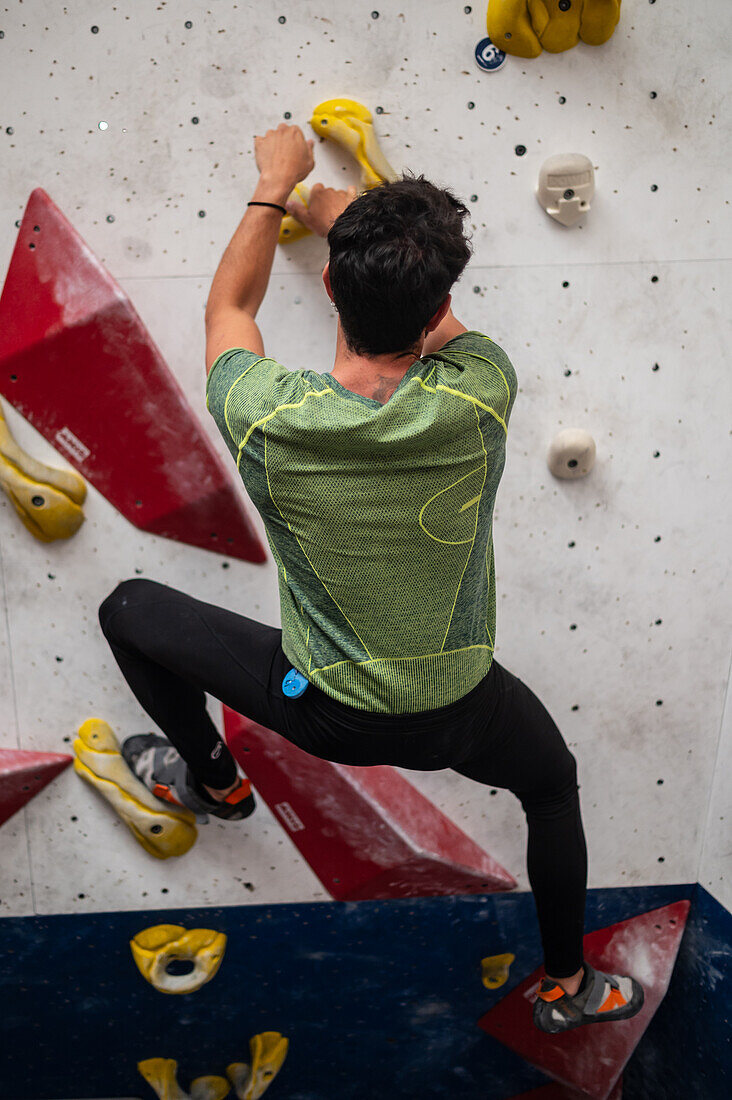 Junger Mann in den Zwanzigern beim Klettern an einer Kletterwand in einer Halle