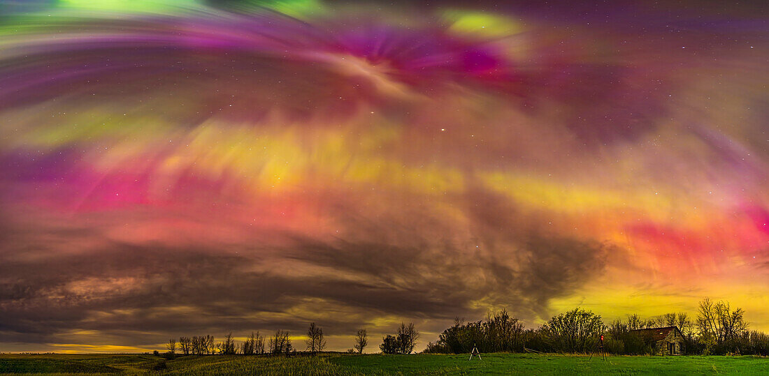 This is a panorama of a substorm outburst during the great May 10, 2024 display of Northern Lights, here creating an overhead corona with rays converging to the magnetic zenith (south of the true zenith), and amid clouds. The rays show a rich mix of oxygen greens and reds, as well as nitrogen blues blending to create purples. Some green and red are mixing to make yellows.