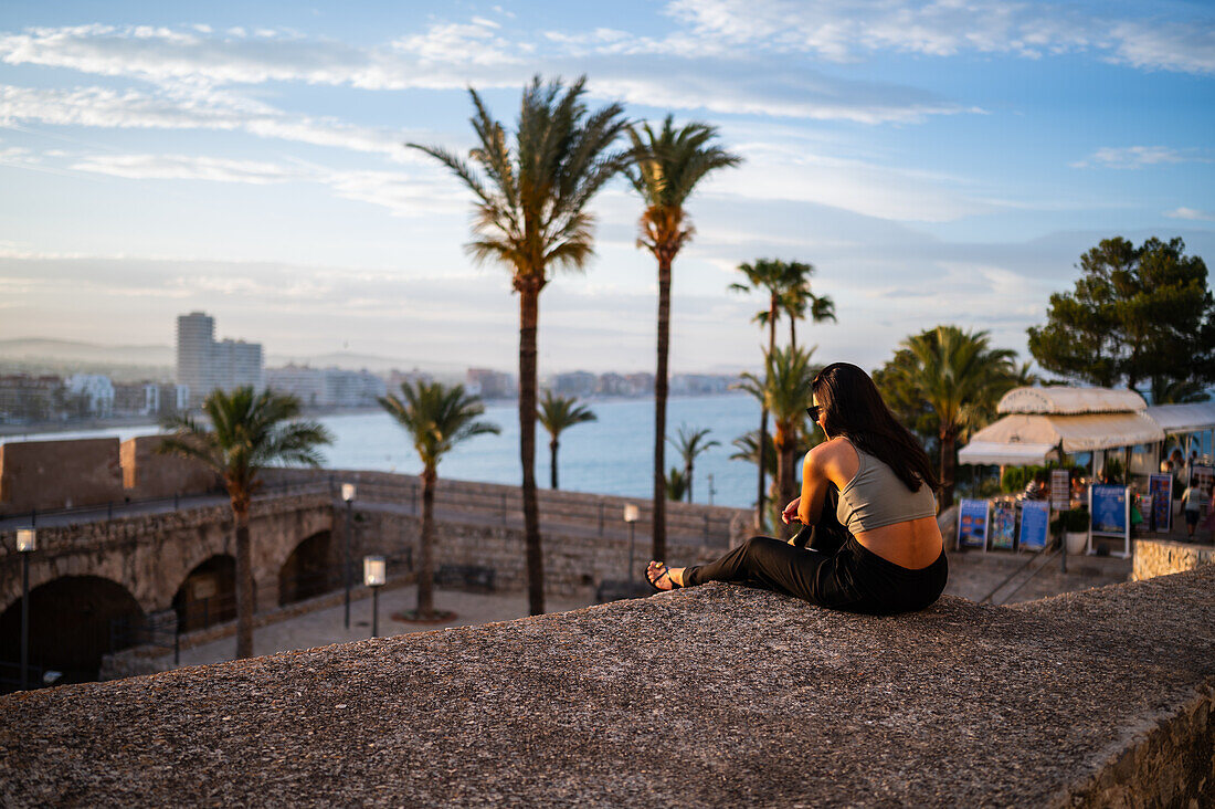 Young woman enjoying the sunset from the city walls of Papa Luna castle in Peñiscola, Castellon, Valencian Community, Spain