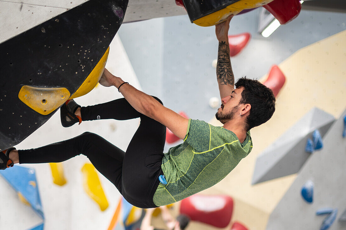 Junger Mann in den Zwanzigern beim Klettern an einer Kletterwand in einer Halle