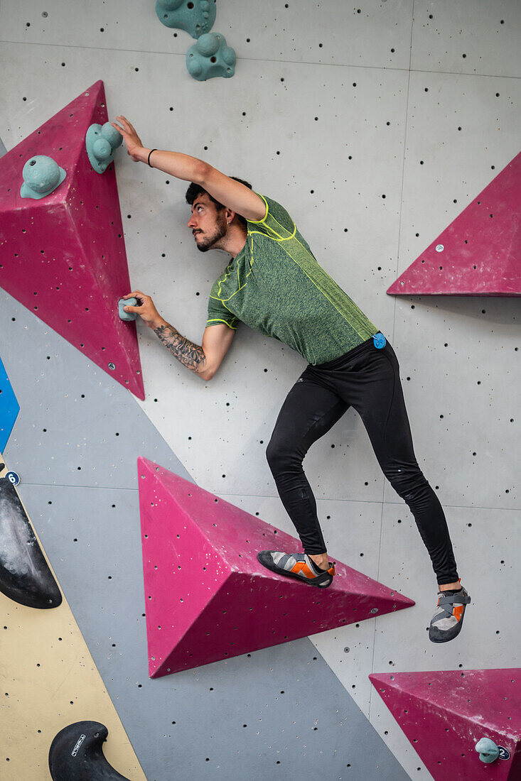 Junger Mann in den Zwanzigern beim Klettern an einer Kletterwand in einer Halle