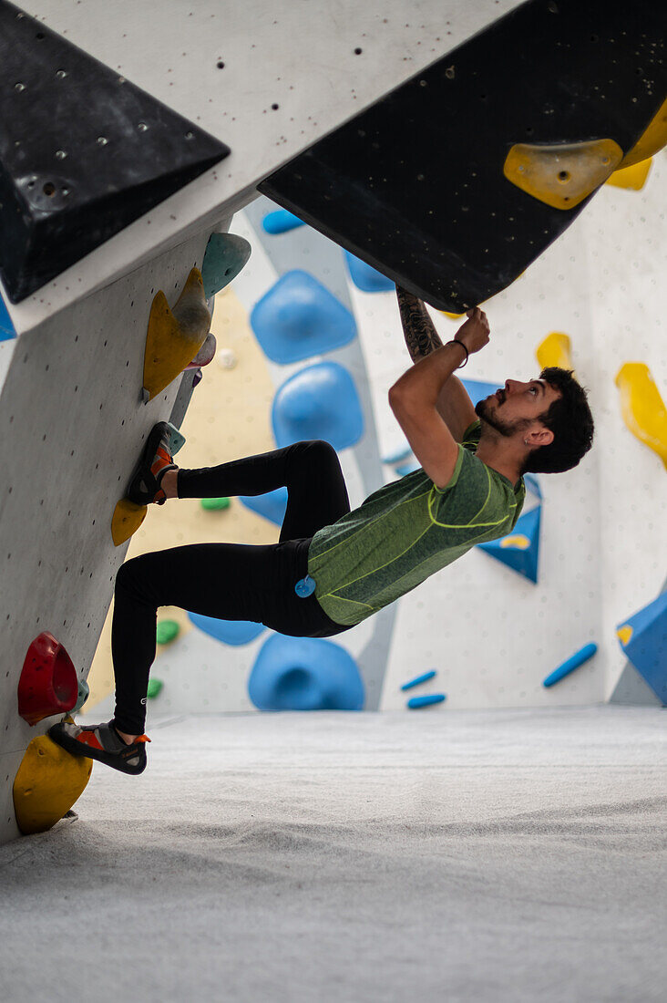 Junger Mann in den Zwanzigern beim Klettern an einer Kletterwand in einer Halle