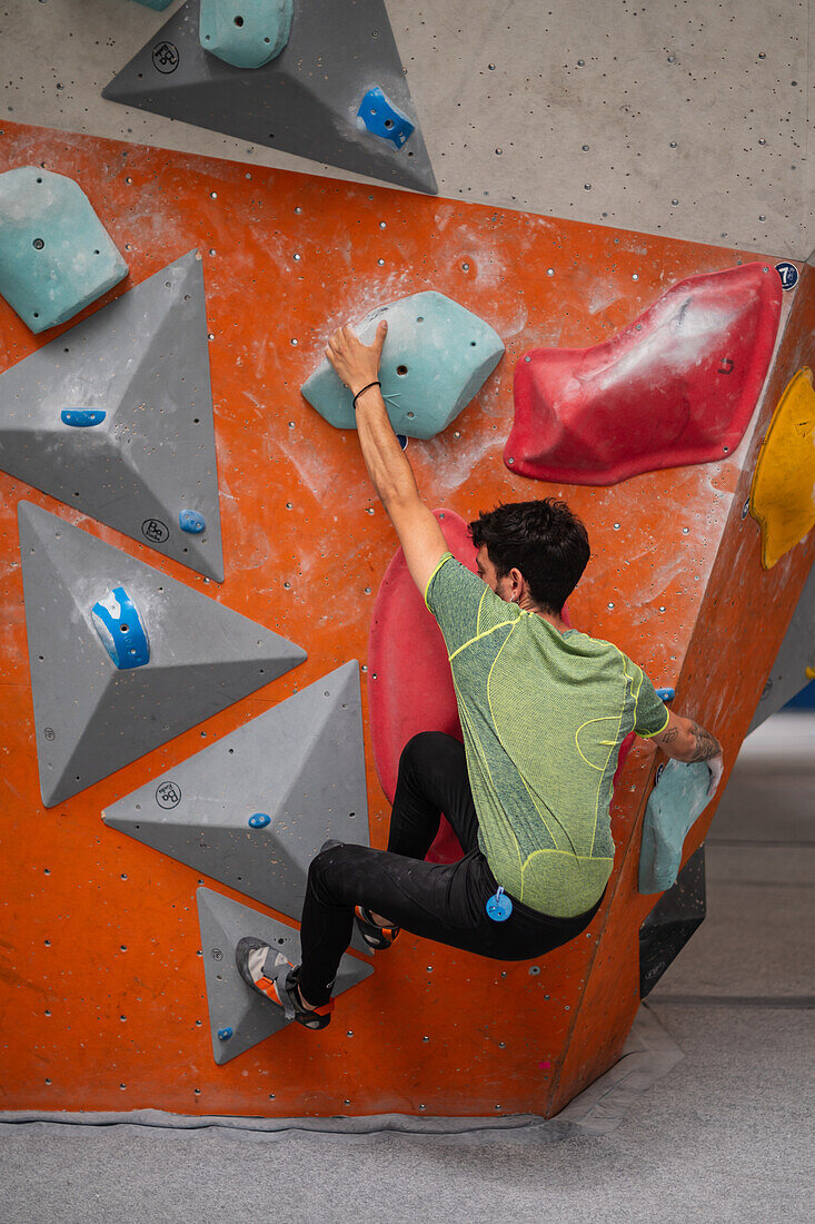 Young man in his twenties climbing on a climbing wall indoors