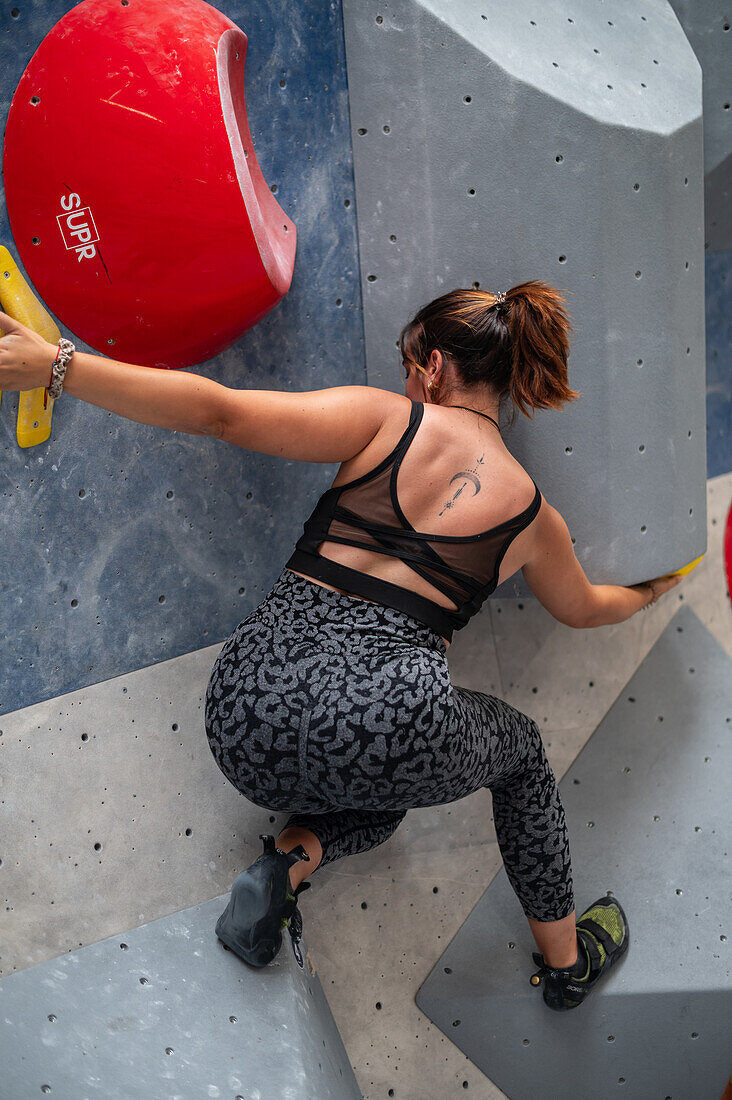 Young man in her twenties climbing on a climbing wall indoors