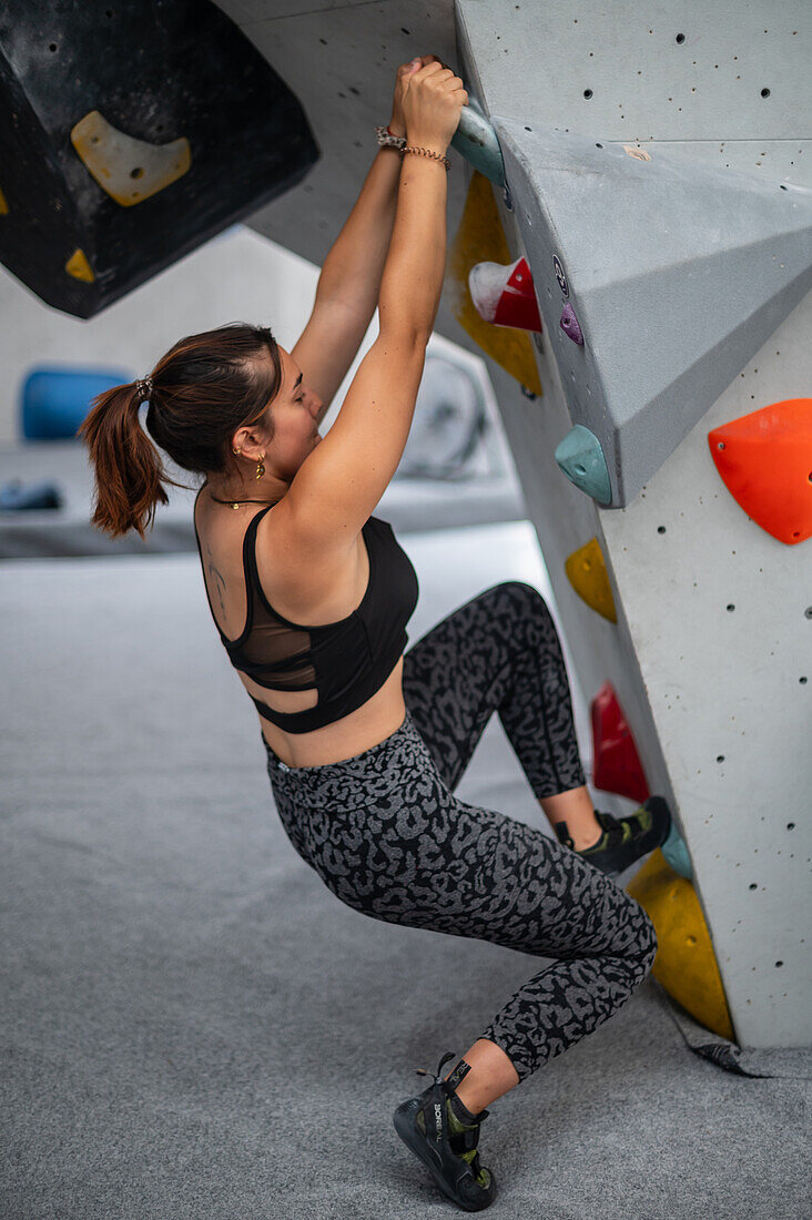 Young man in her twenties climbing on a climbing wall indoors