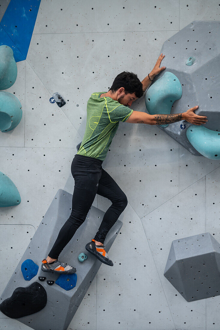 Junger Mann in den Zwanzigern beim Klettern an einer Kletterwand in einer Halle