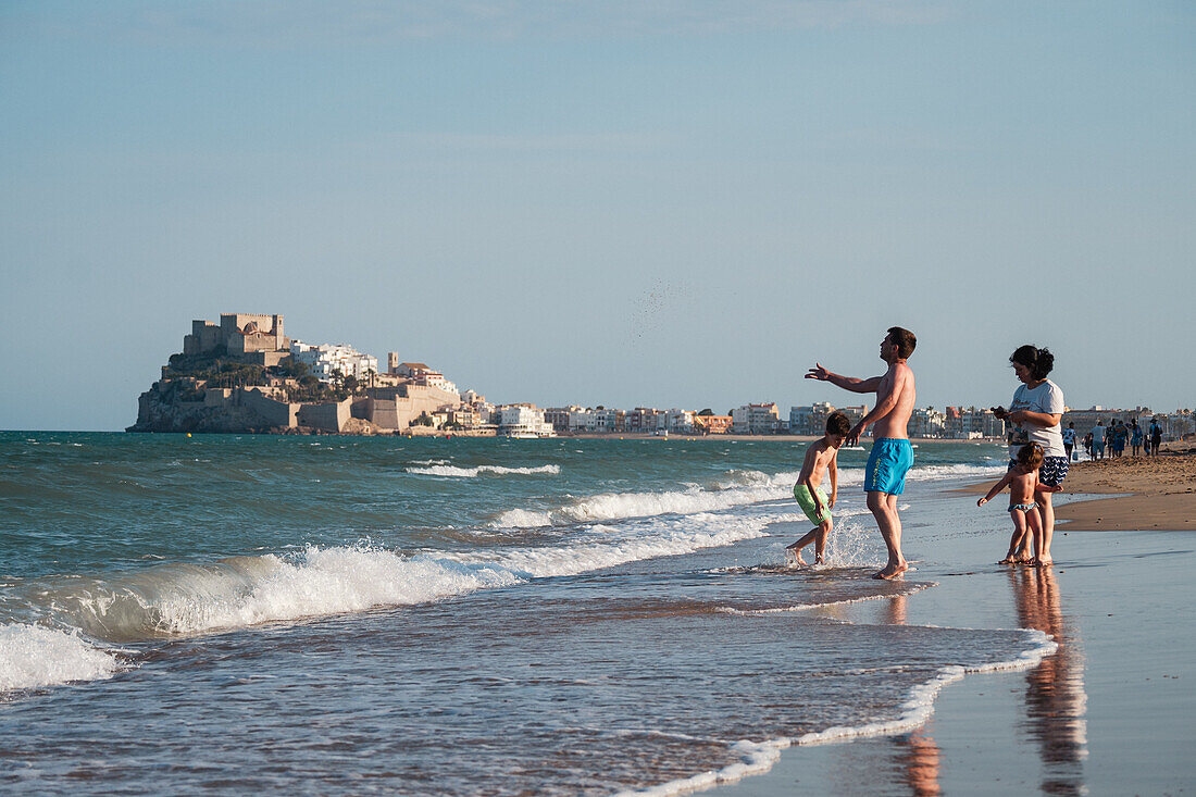 Familie am Strand und Blick auf die Burg Papa Luna in Peñiscola, Castellon, Valencianische Gemeinschaft, Spanien