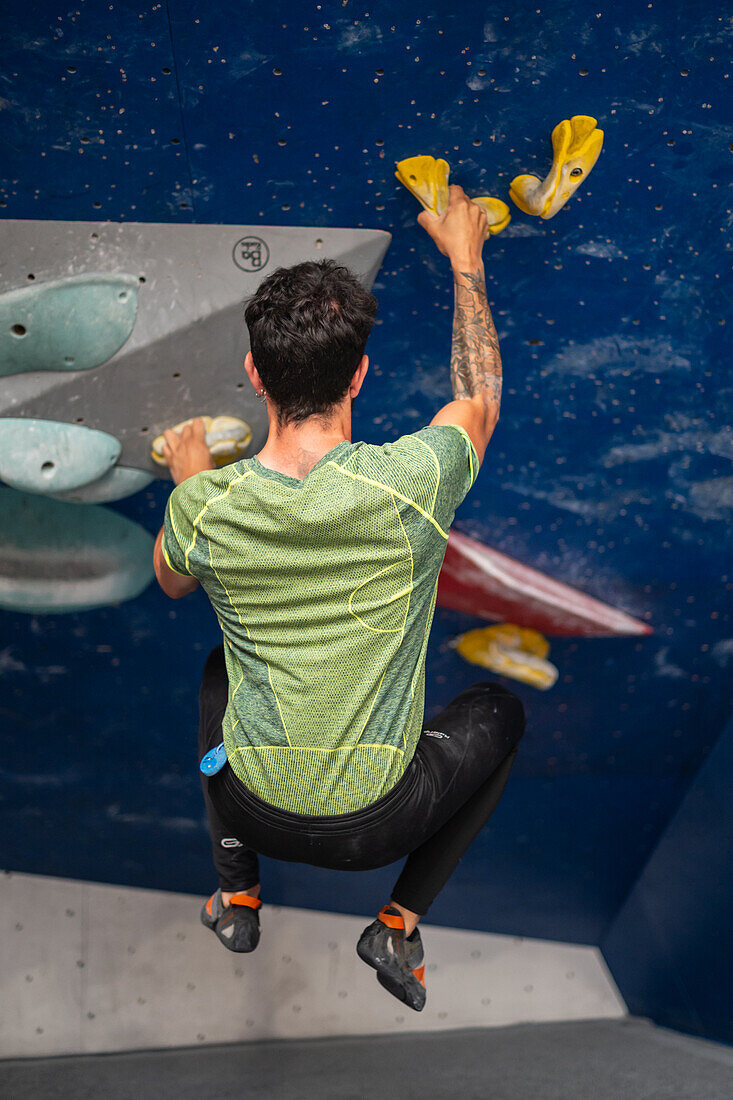 Young man in his twenties climbing on a climbing wall indoors