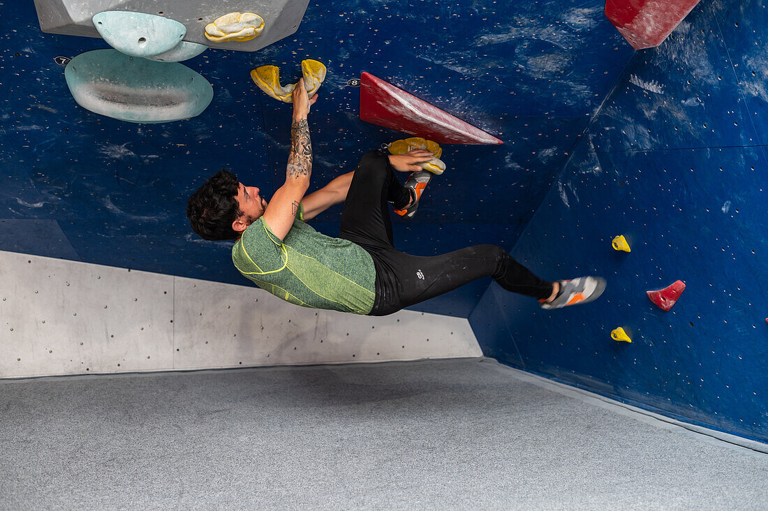 Junger Mann in den Zwanzigern beim Klettern an einer Kletterwand in einer Halle