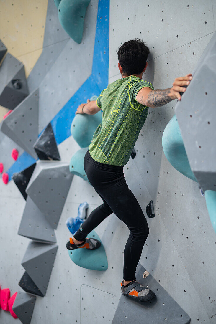 Junger Mann in den Zwanzigern beim Klettern an einer Kletterwand in einer Halle